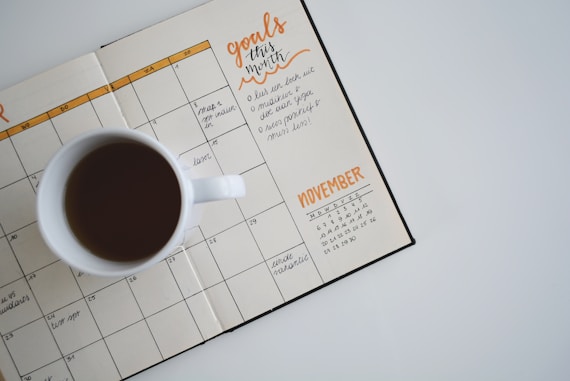 White coffee mug placed on an open planner with handwritten goals and a November calendar