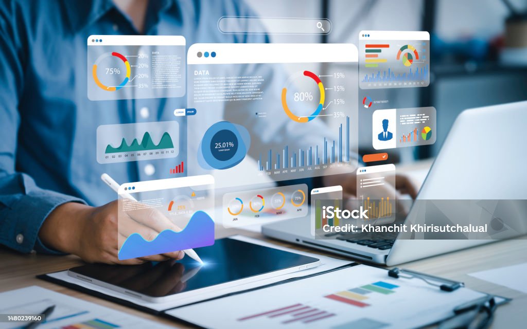 Person using a tablet with floating digital data visualizations and charts next to a laptop