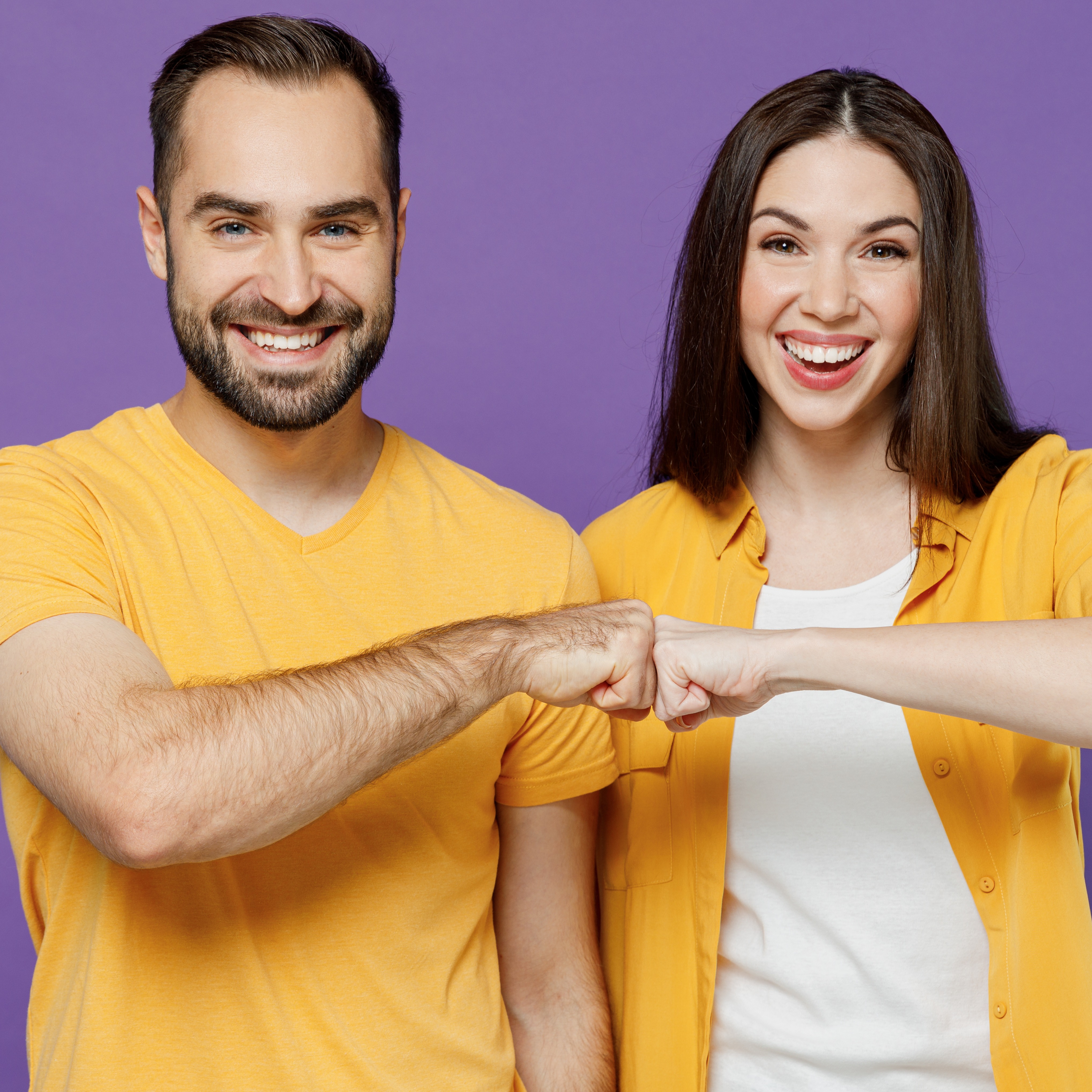 Young Smiling Cheerful Happy Couple Two Friends Family Man Woman Together in Yellow Casual Clothes Looking Camera Giving a Fist Bump in Agreement Isolated on Plain Violet Background Studio Portrait.